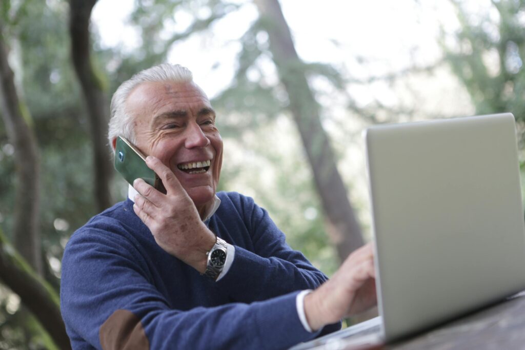 pexels-photo-3783348-3783348 Happy senior man talking on phone and using laptop outdoors.