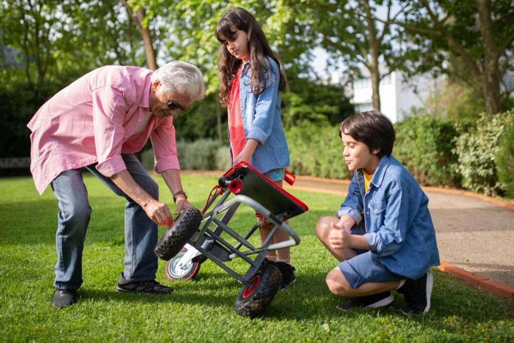 pexels-photo-7854103-7854103 An elderly man assists two children in fixing a garden cart outdoors, showcasing family bonding and teamwork.